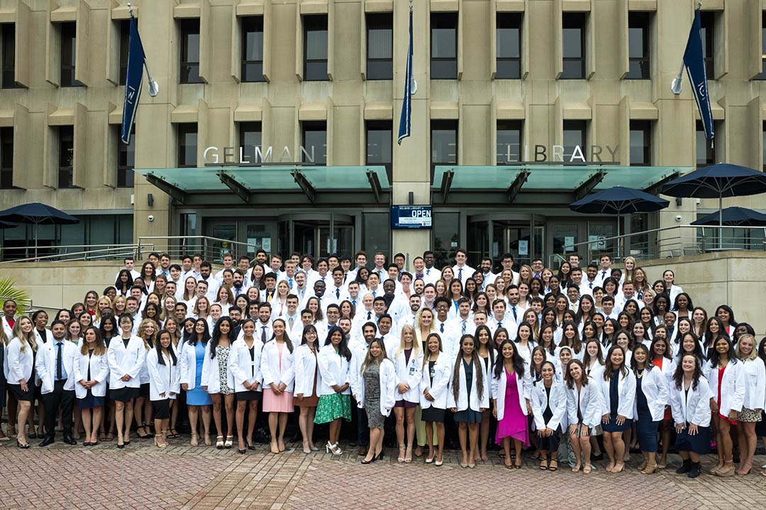 Large group of GW med students in their new white coats in front of Gelman Library