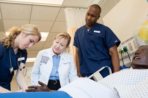 2 GW nursing students practice with a professor on a dummy